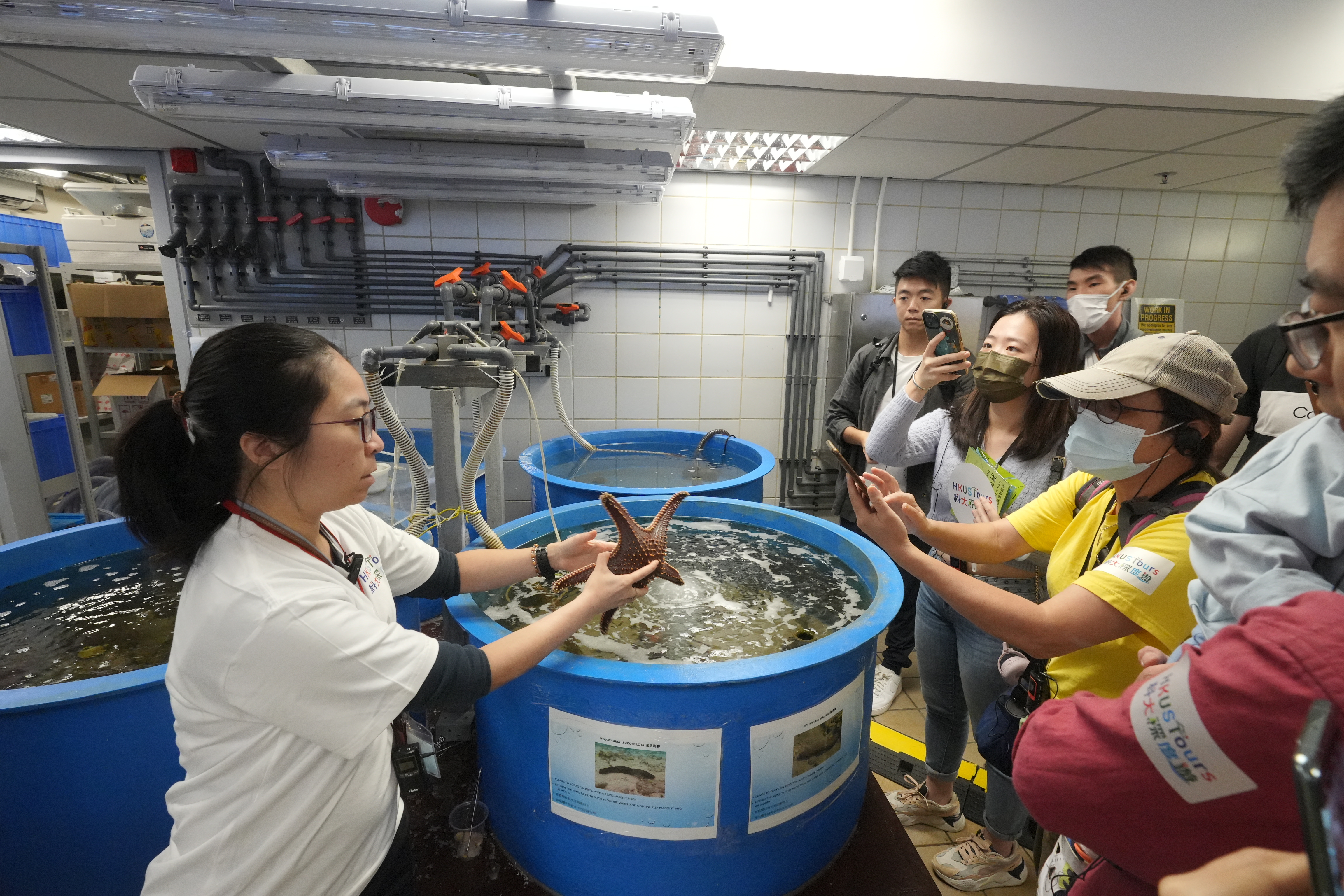 熱愛海洋的Bernadette（左一）為參加者介紹科大海濱，和周邊的海洋生物教學和研究設施。在實驗中心，Bernadette亦特意展示海星、馬蹄蟹等各種海洋生物，講解香港海洋生態的歷史和現況，並讓參加者近距離觀賞和接觸。  Bernadette說看到大家非常興奮，也踴躍發問及留影，令她感到由衷的滿足。