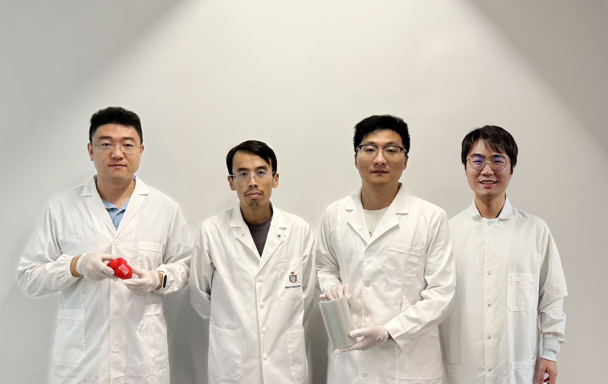 科大機械及航空航天工程學系副教授楊徵保教授（左二）與論文的三位共同第一作者——科大博士後研究員李學木博士（右二，手持一卷列印的甘氨酸薄膜）、城大博士畢業生張卓敏博士（右一）及城大博士生鄭毅（左一，手持列印出的甘氨酸壓電貼片）。